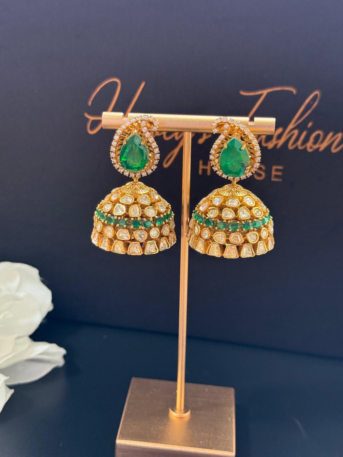 Gold and emerald green earrings on a stand with a dark background