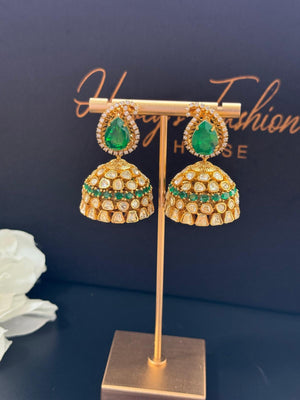 Gold and emerald green earrings on a stand with a dark background