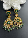 Ornate gold and green earrings on a dark surface with white flowers in the background