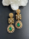 Gold and green earrings on a dark surface with white flowers in the background