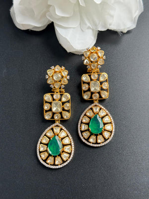 Gold and green earrings on a dark surface with white flowers in the background