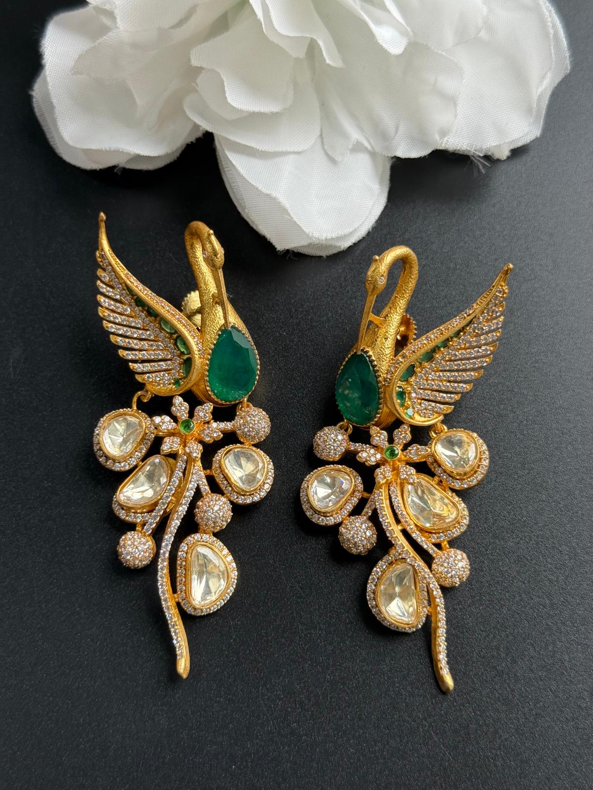 Gold earrings with green and clear gemstones on a dark background