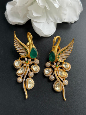Gold earrings with green and clear gemstones on a dark background