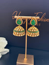 Gold and emerald green earrings on a stand with a dark background