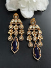 Pair of gold and blue earrings on a dark surface with white flowers in the background